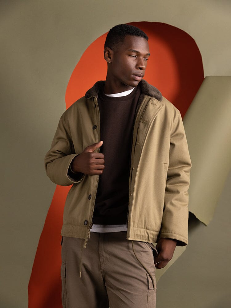 A person wearing a brown shirt and the 1940s N-1 Deck Jacket in khaki by Alpha Industries, featuring a cotton shell.