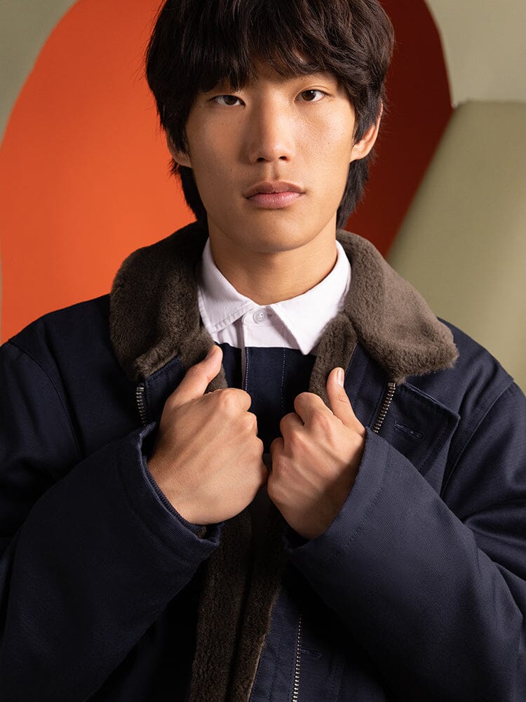 A person wearing the 1940s N-1 Deck Jacket in navy blue by Alpha Industries, featuring a dark design with a fur collar that evokes classic US Navy styles.