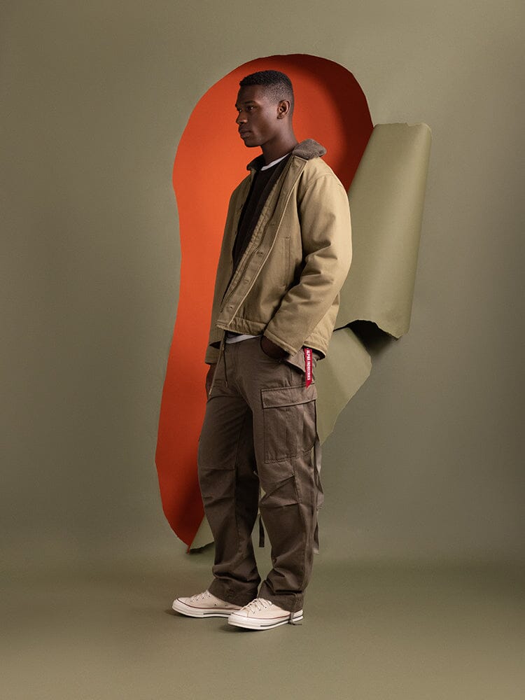 A person stands in profile wearing the 1940s N-1 Deck Jacket in khaki by Alpha Industries.