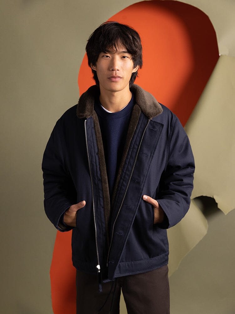 A person dons the 1940s N-1 Deck Jacket in navy blue by Alpha Industries, featuring a cotton shell, reminiscent of the classic style of the US Navy.