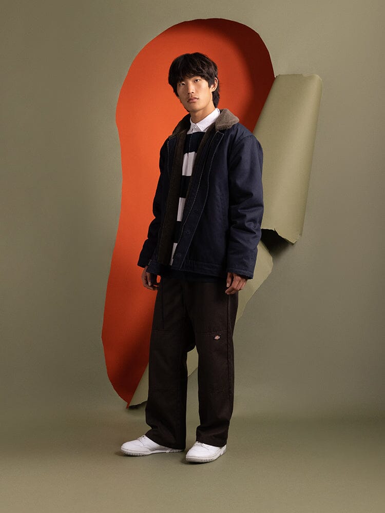 A person wearing the 1940s N-1 Deck Jacket in navy blue by Alpha Industries, paired with a striped shirt and dark pants.