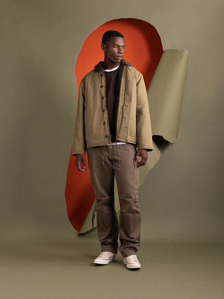 A person stands wearing the 1940s N-1 Deck Jacket in khaki by Alpha Industries, featuring a cotton shell.