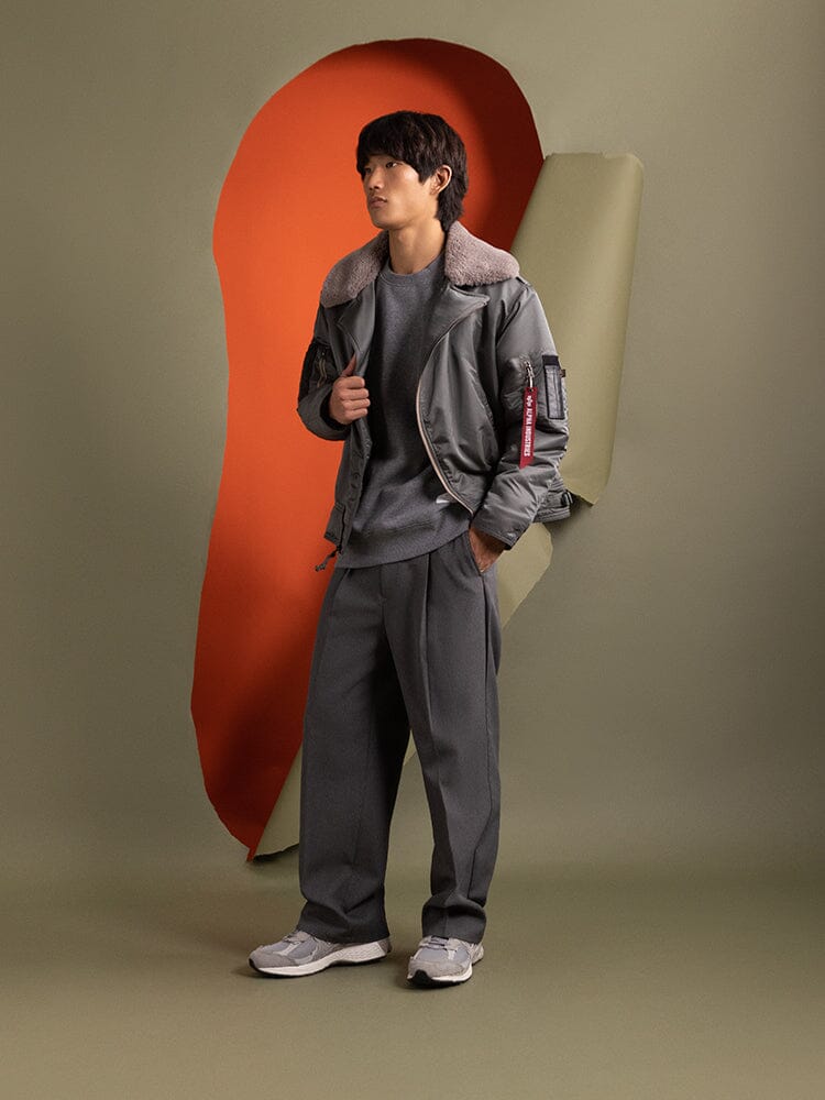 A person wearing the stylish 1960s RCAF Canadian Airforce Type III Jacket in field gray by Alpha Industries, featuring utility pockets and matching pants.