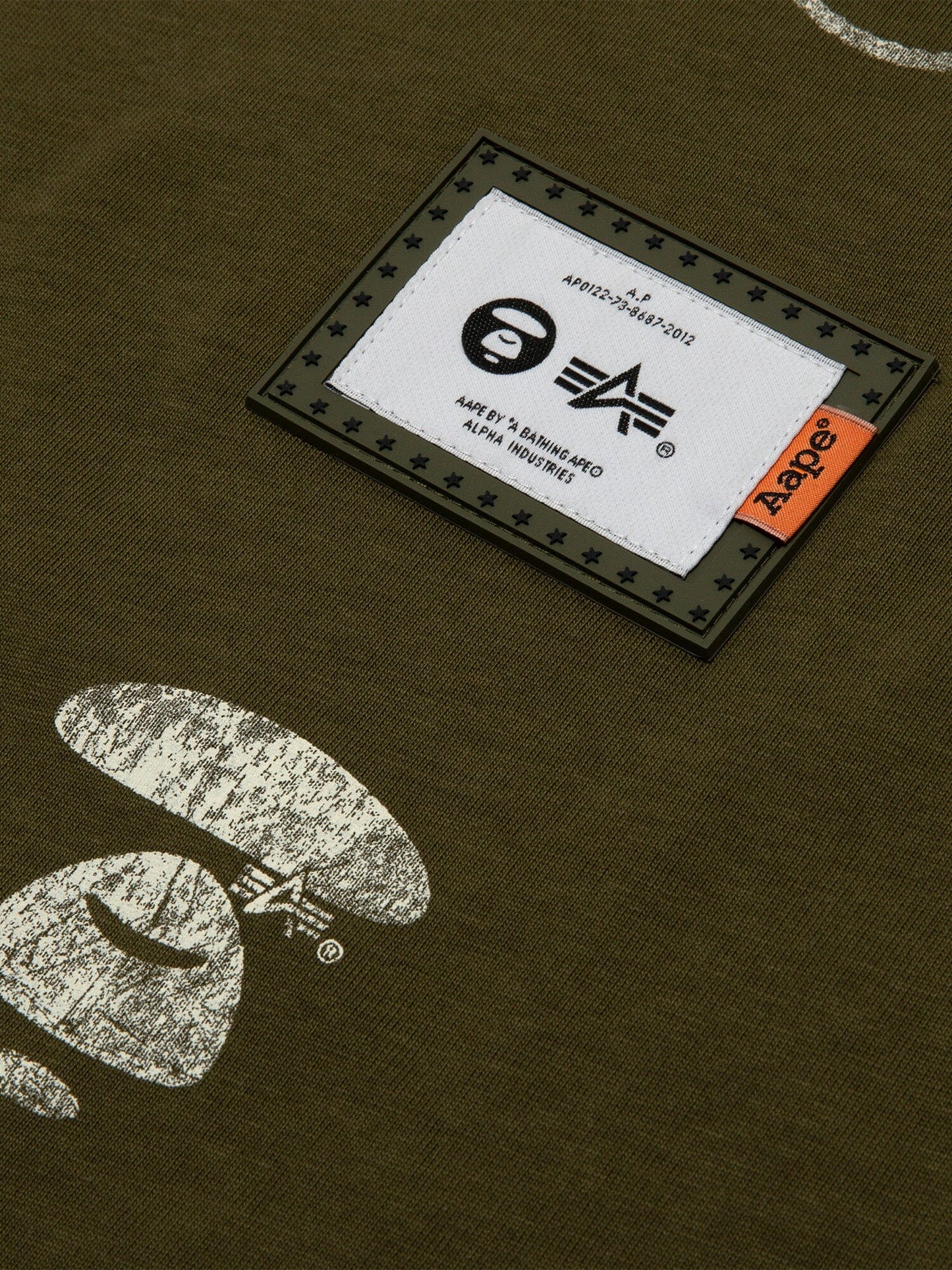 Close-up of the Alpha Industries Green AAPE X Alpha Somewhere In Universe Tee with White Prints, Rectangular Patch with Logos.