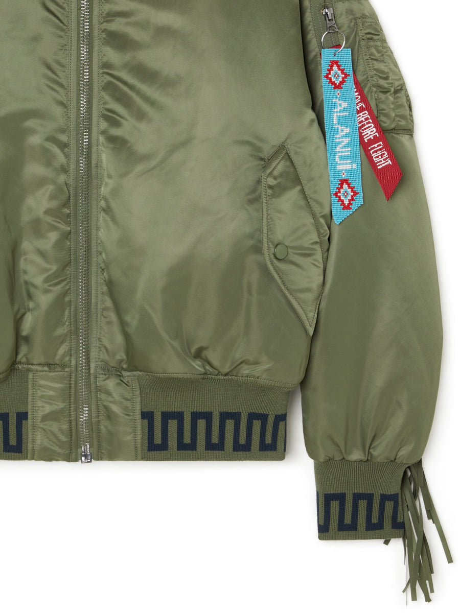 Alanui X Alpha Industries MA-1 Jacket, olive green fabric, geometric black pattern on hem and cuffs, zippered sleeve pocket, patchwork bandana lining, red and blue keychain tags.