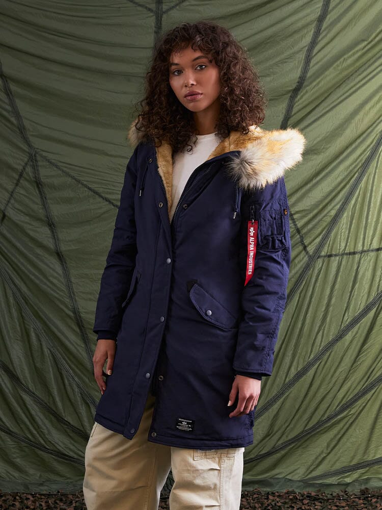 An individual wearing the Elyse Gen II Parka W in navy blue from Alpha Industries, featuring a faux fur trim.
