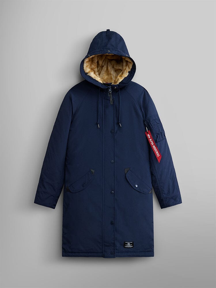 The Elyse Gen II Parka W by Alpha Industries is displayed. This navy blue hooded parka comes with button and zip closures, a distinct red tag on the left sleeve, and features a faux fur-trimmed hood.