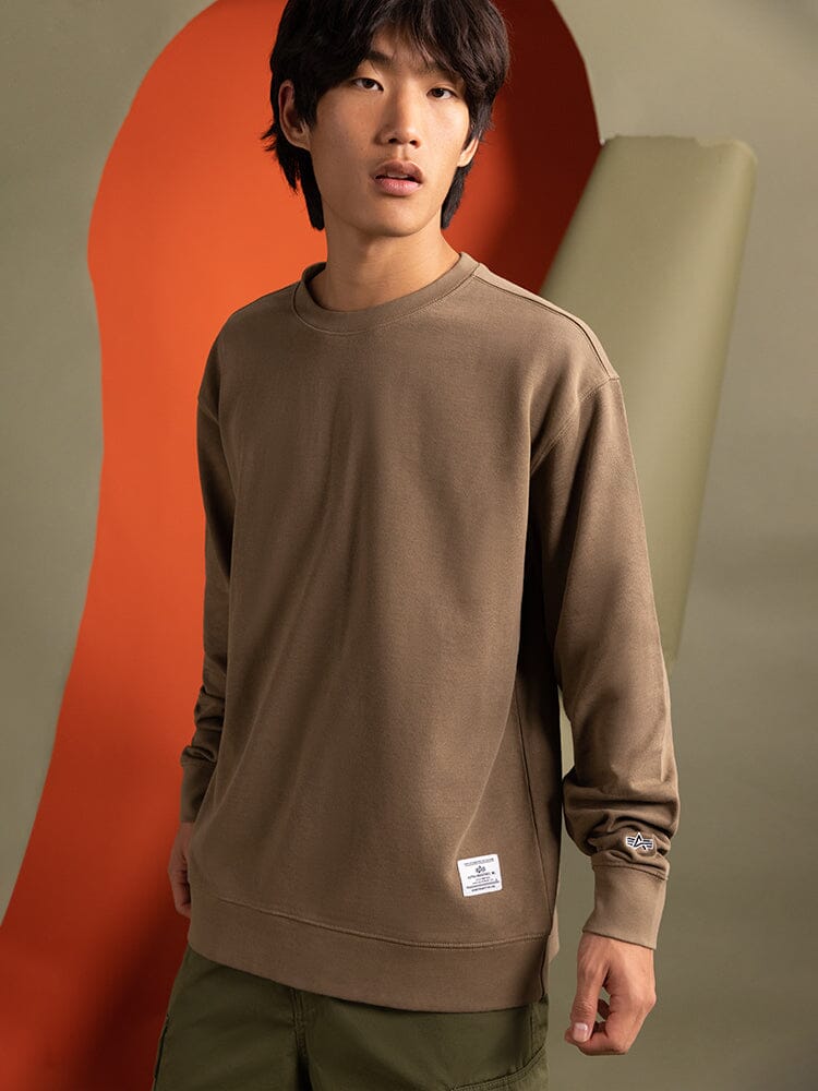 A person wearing the Essential Crewneck from Alpha Industries stands.