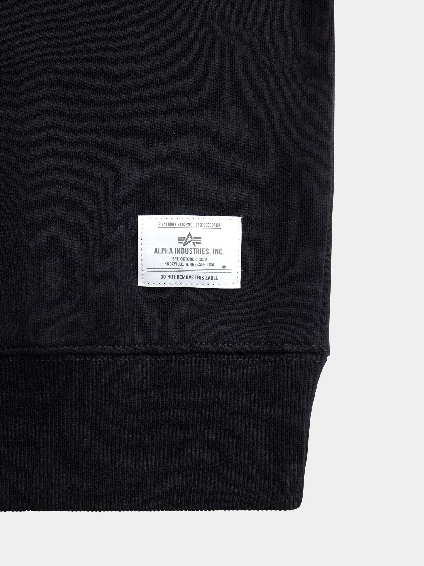 Black Alpha Industries Essential Crewneck with white rectangular label near ribbed hem, soft cotton blend.
