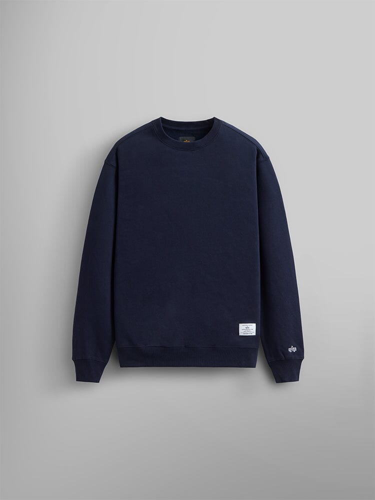 The Essential Crewneck by Alpha Industries is a plain black unisex sweatshirt made from a cotton blend. It features a small white label on the lower left side.