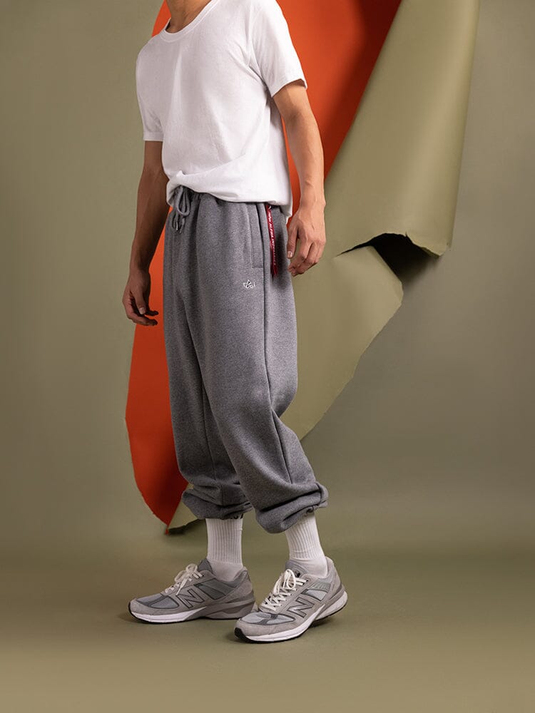 A person in an Alpha Industries White T-Shirt and Essential Sweatpants, crafted from soft cotton fabric, wears gray sneakers and white socks.