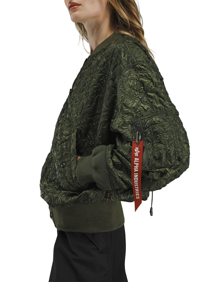 Alpha Industries L-2B Bubble Flight Jacket W in olive green with textured shell, red Remove Before Flight sleeve tag, and black pants.