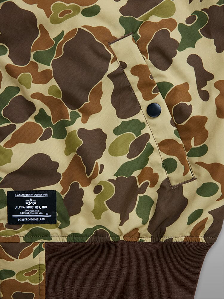 Close-up of an Alpha Industries L-2B Skymaster Gen II Bomber Jacket showcasing its brown, green, and tan camouflage patterns. This nylon jacket is water-resistant and features a black label with white text near the hem.