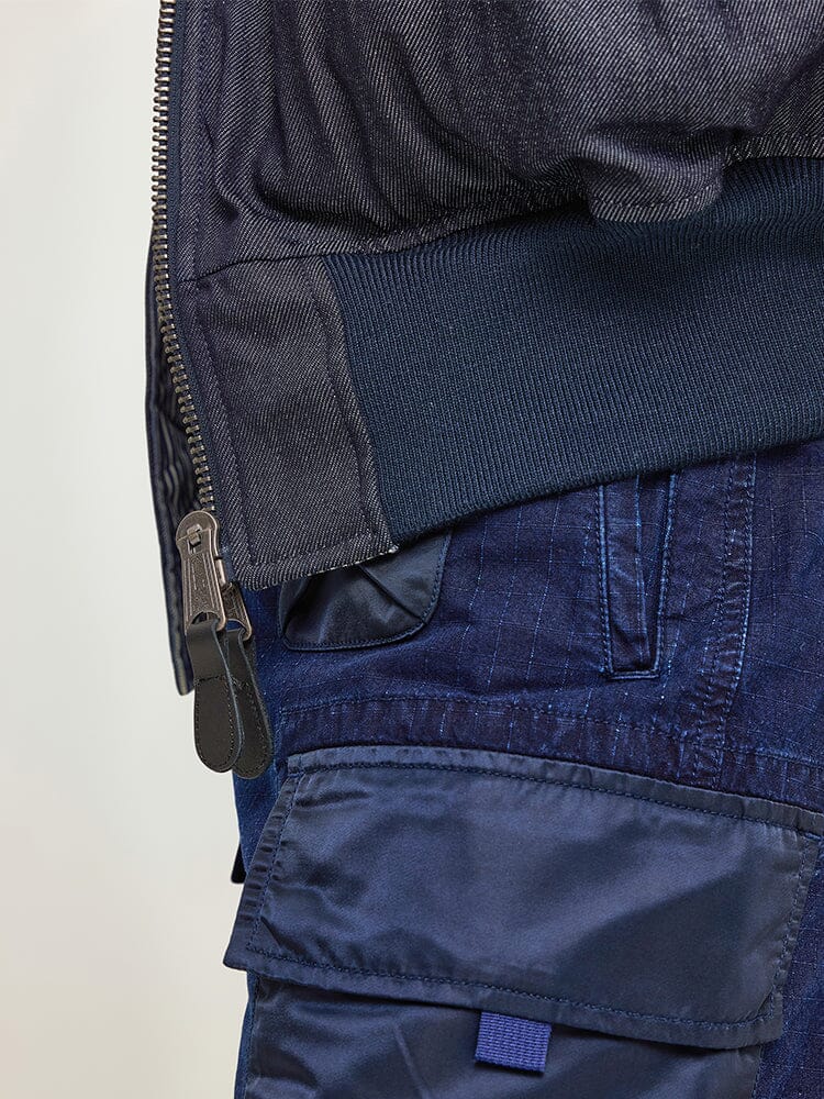 Close-up of the Alpha X Lee Reversible MA-1 Jacket in dark blue with a visible zipper, paired with navy cargo pants featuring pockets from Alpha Industries.