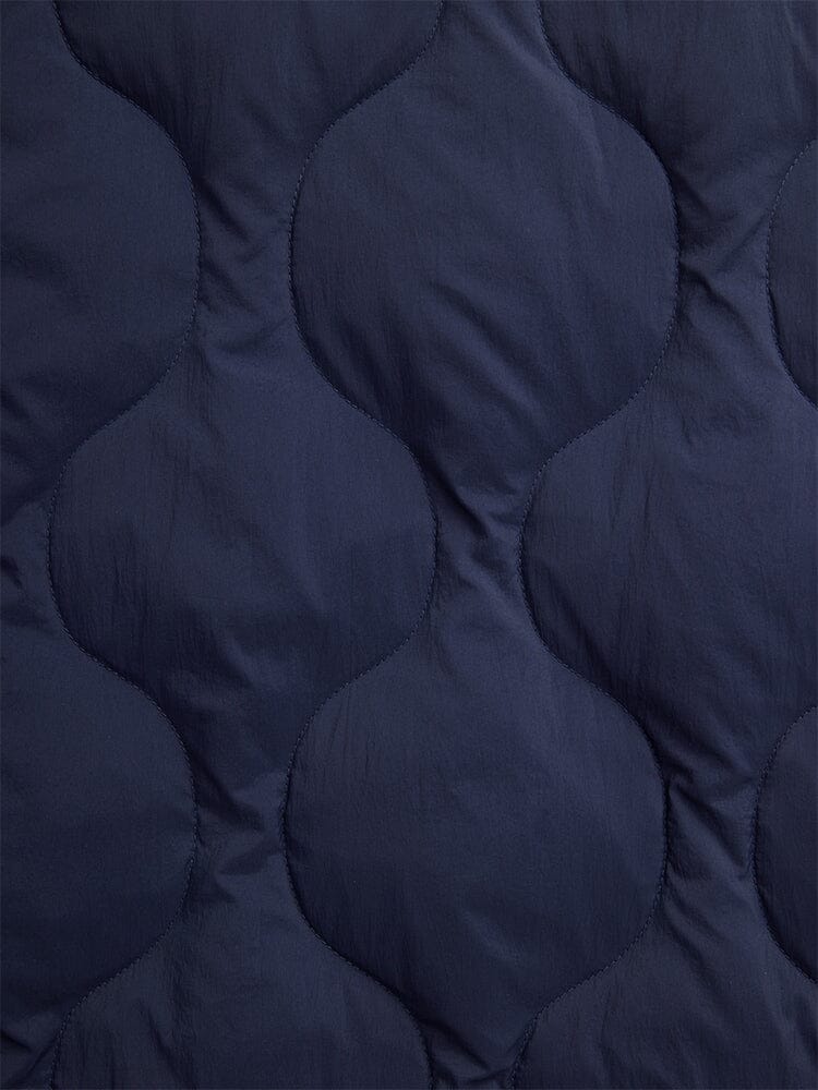 Close-up of the Lightweight Quilted Down Jacket by Alpha Industries, showcasing its dark blue fabric with a wave-like quilted pattern, providing a luxurious down-filled feel.