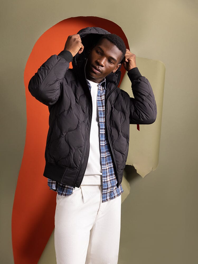 Dressed in the Lightweight Quilted Down Jacket in balck by Alpha Industries, a person adjusts the detachable hood.