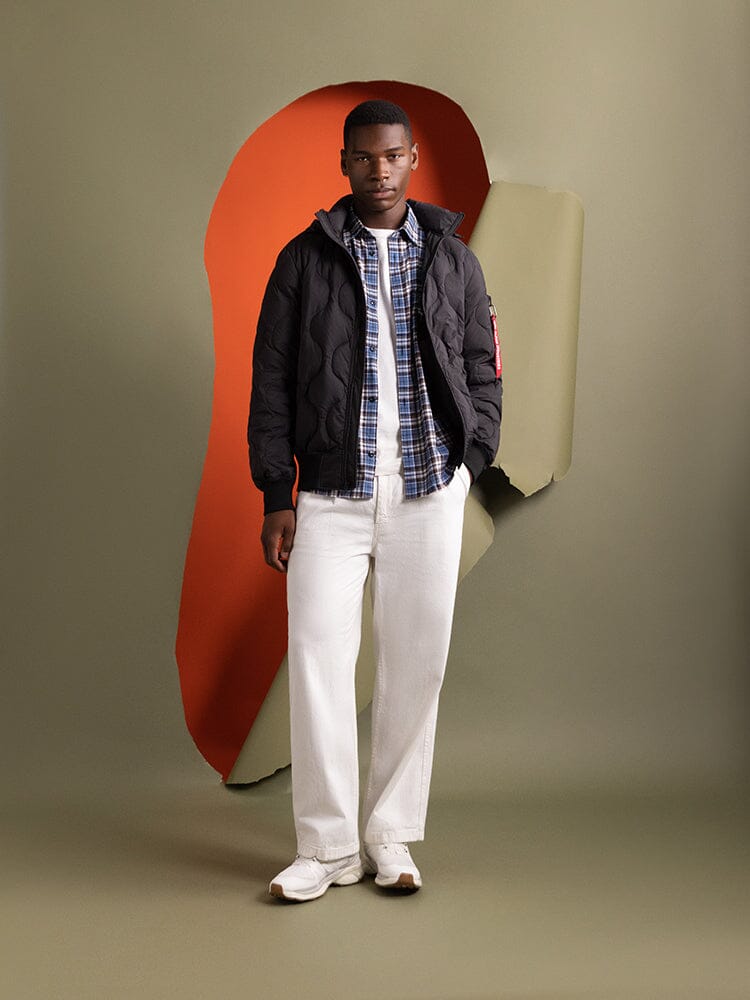 A man standing wearing an Alpha Industries Lightweight Quilted Down Jacket in black.