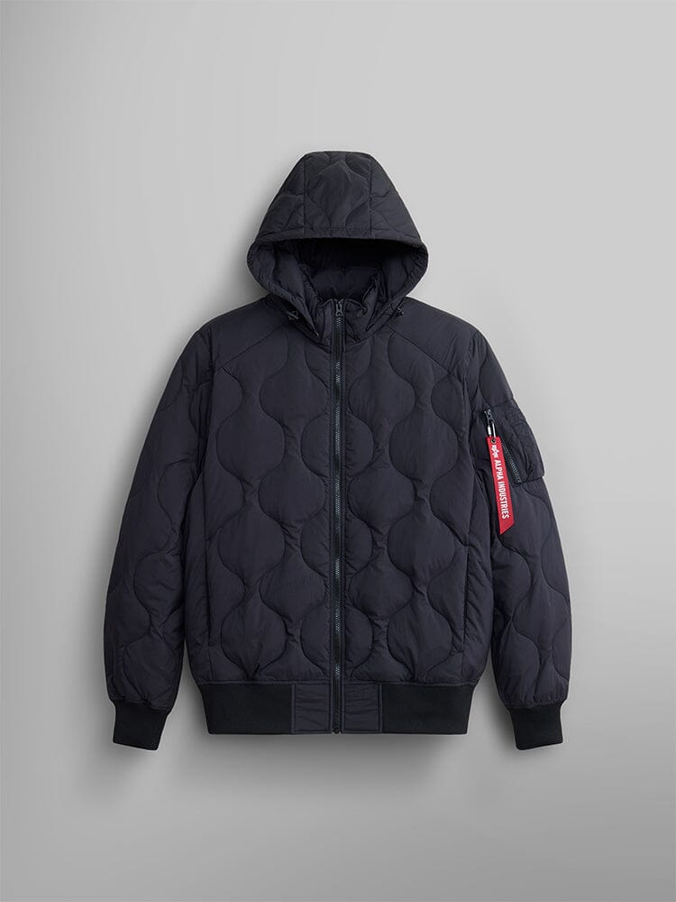 The Lightweight Quilted Down Jacket by Alpha Industries features a black design with down filling, removable hood, ribbed cuffs, front zipper, and a distinctive red Alpha Industries tag on the sleeve.