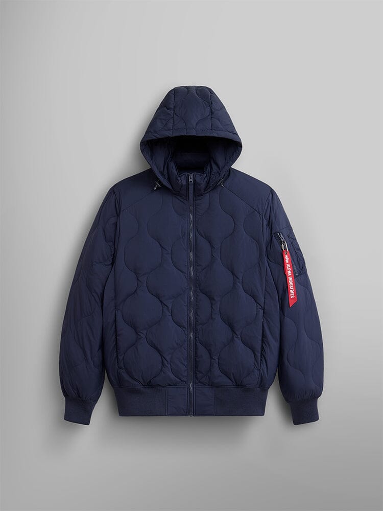 A replica blue lightweight quilted down jacket from Alpha Industries, featuring a removable hood, a zippered front, and a red Remove Before Flight tag on the sleeve.