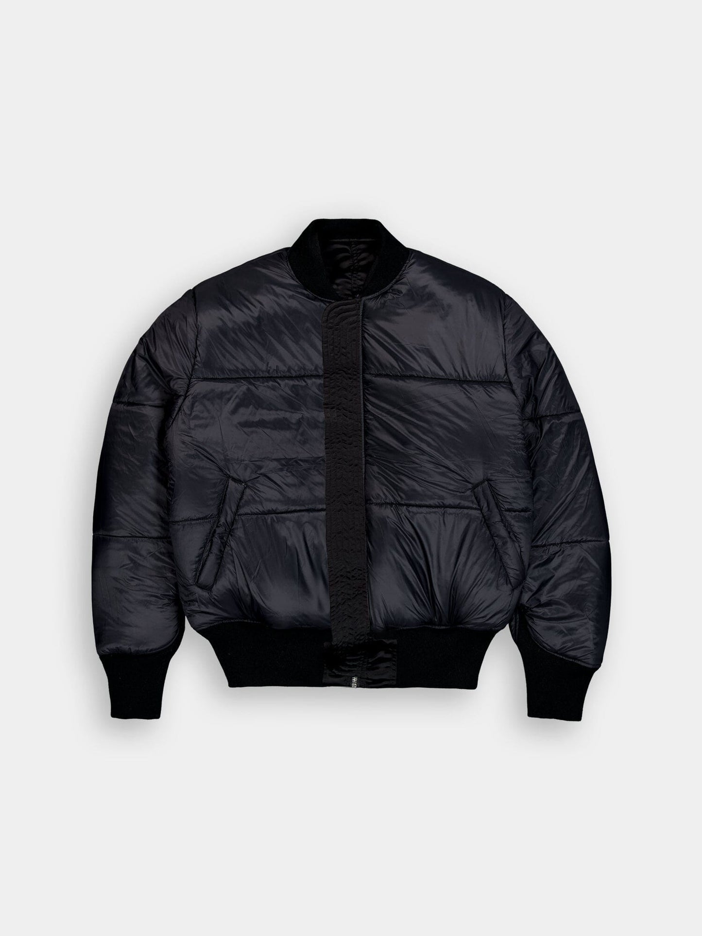 Alpha Industries MA-1 jacket in black with puffer-style bomber design, ribbed cuffs and hem, front zipper closure, and side pockets.