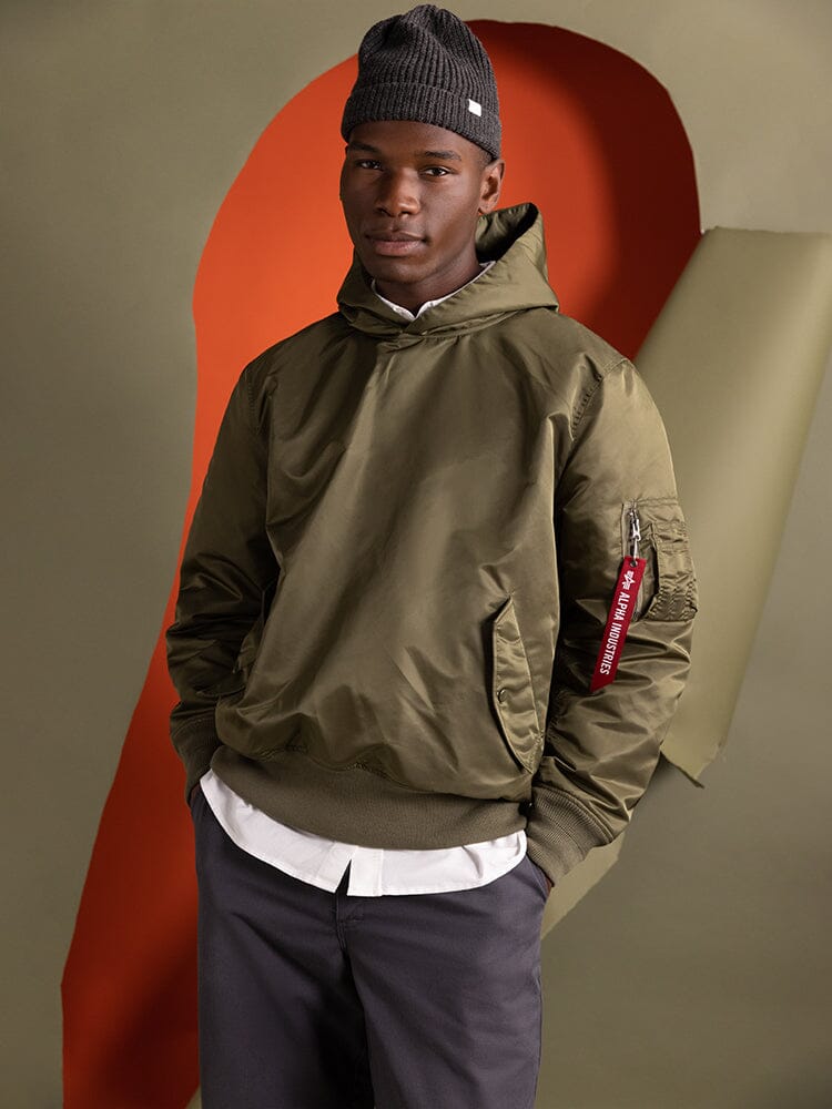 A person wearing the Alpha Industries Pull-Over MA-1 Jacket Hoodie, characterized by its green color and utility pockets.