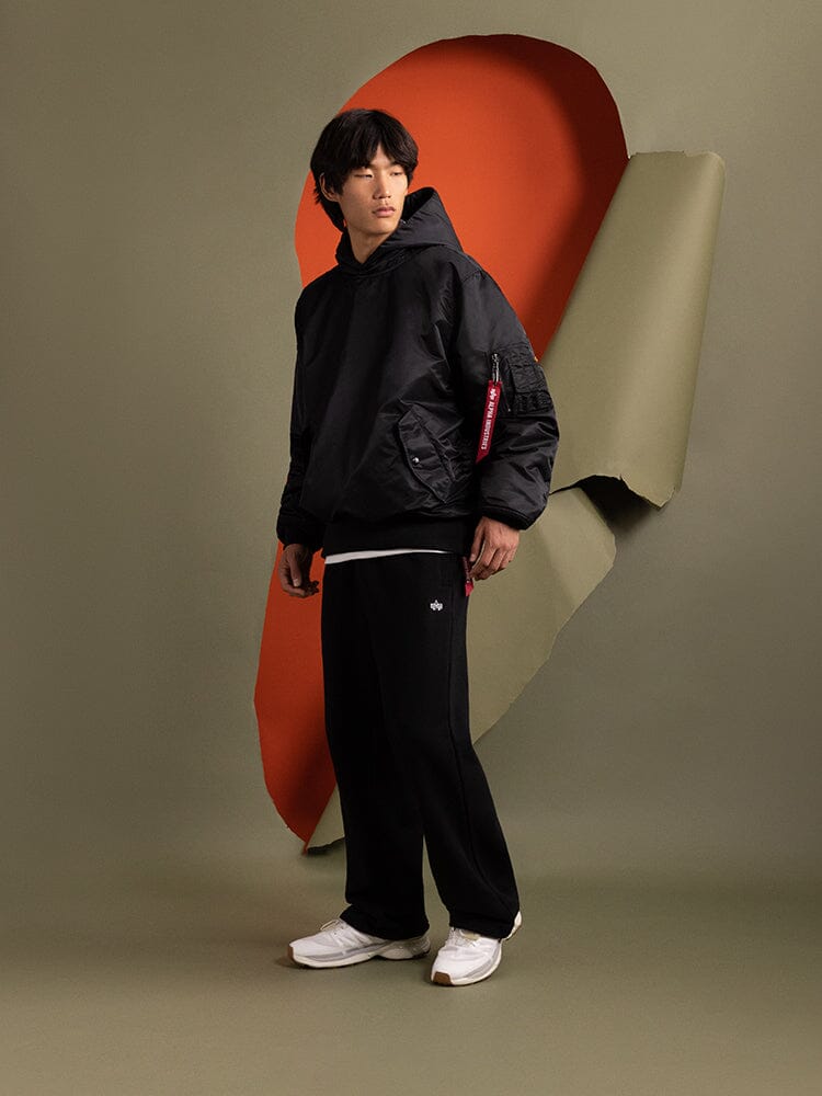 A person wearing the Alpha Industries Pull-Over MA-1 Jacket Hoodie in black evokes the vibrant layers often found in an iconic flight jacket known for its utility pockets.