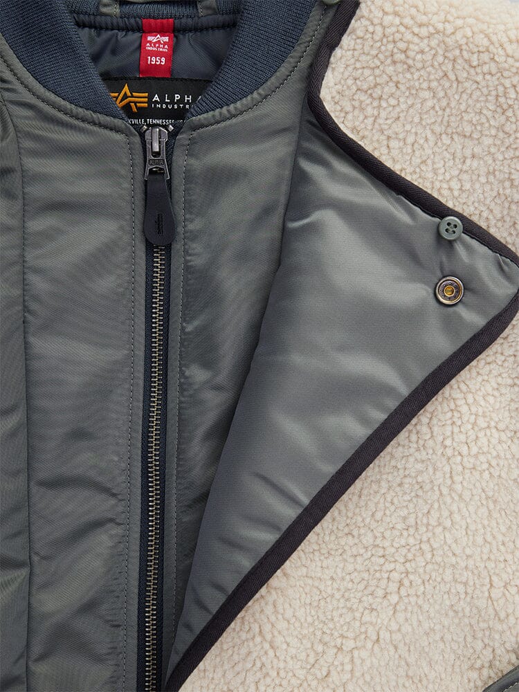 Close-up of the Women's B-15 Sherpa Hybrid Bomber Jacket by Alpha Industries, this gray jacket showcases a fleece lining, visible asymmetrical zipper, and a buttoned flap.