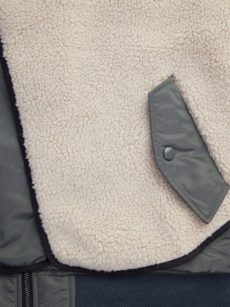 Close-up of the Women's B-15 Sherpa Hybrid Bomber Jacket from Alpha Industries, spotlighting textured cream sherpa fleece paneling complemented by a green fabric pocket with a side button.