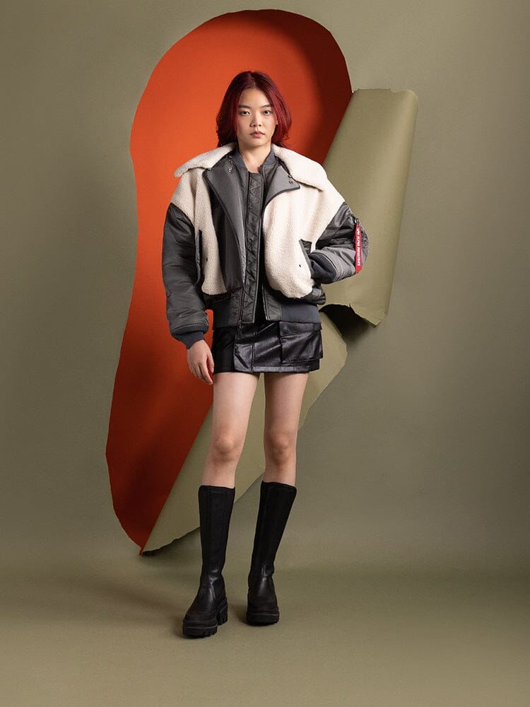 A person stands wearing the Women's B-15 Sherpa Hybrid Bomber Jacket in field gray from Alpha Industries.
