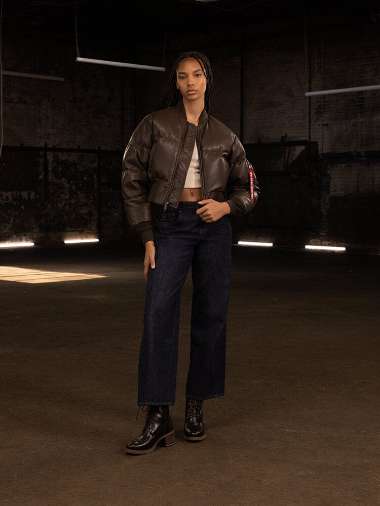 Someone is wearing the Alpha Industries Women's Sierra Faux Leather Short Puffer Jacket, paired with a cropped top, wide-leg jeans, and ankle boots.