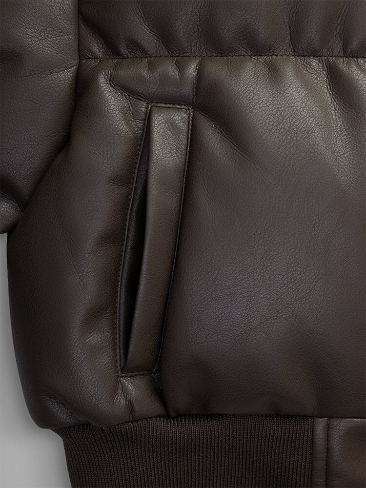 Close-up of the Women's Sierra Faux Leather Short Puffer Jacket by Alpha Industries, showcasing a dark brown color with a pocket and ribbed hem, offering a cropped fit similar to a fashionable puffer bomber jacket.
