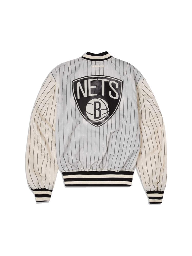 The Brooklyn Nets x Alpha x New Era L-2B Bomber Jacket by Alpha Industries features a vintage design with vertical stripes, a prominent Nets logo on the back, and is embellished with team patches for an authentic look.