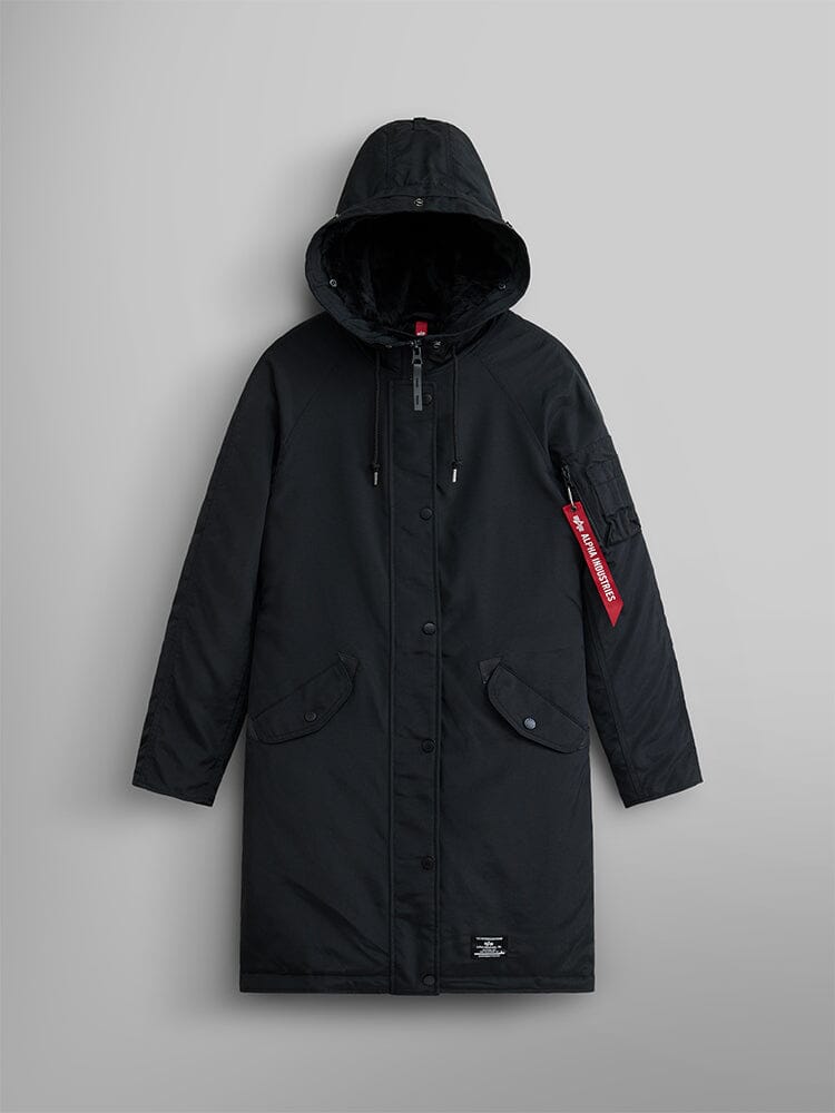 The Elyse Gen II Parka W by Alpha Industries is displayed. This black hooded parka comes with button and zip closures, a distinct red tag on the left sleeve, and features a faux fur-trimmed hood.