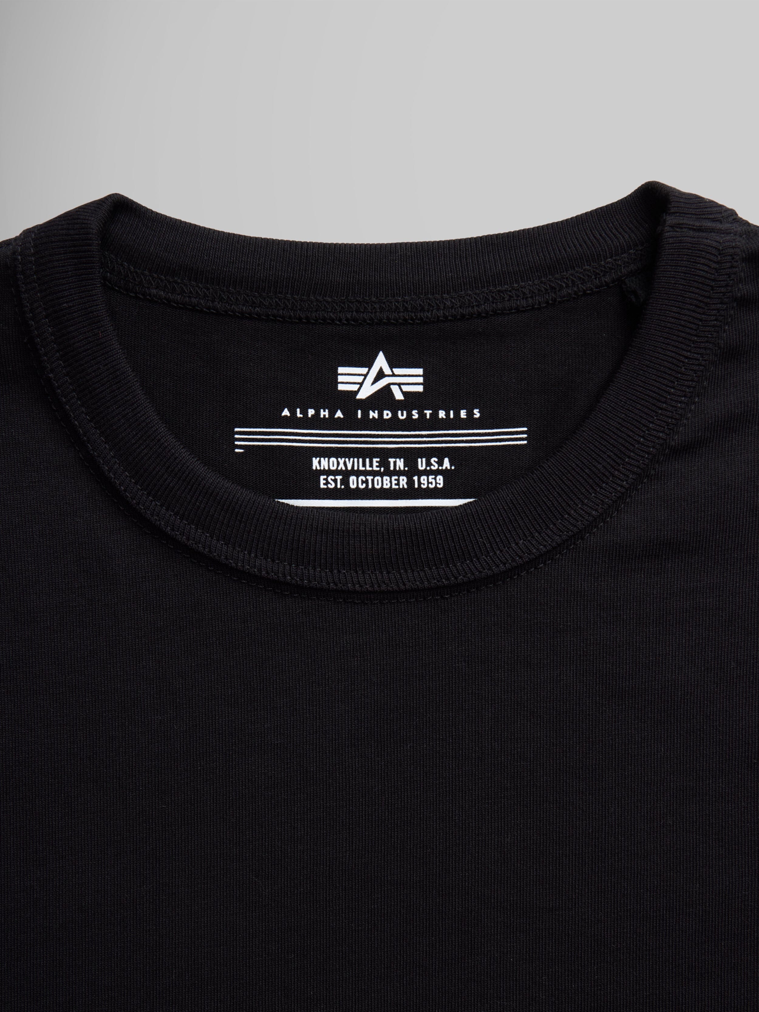 Black Alpha Industries Essential Tee collar and label with brand logo and establishment details.