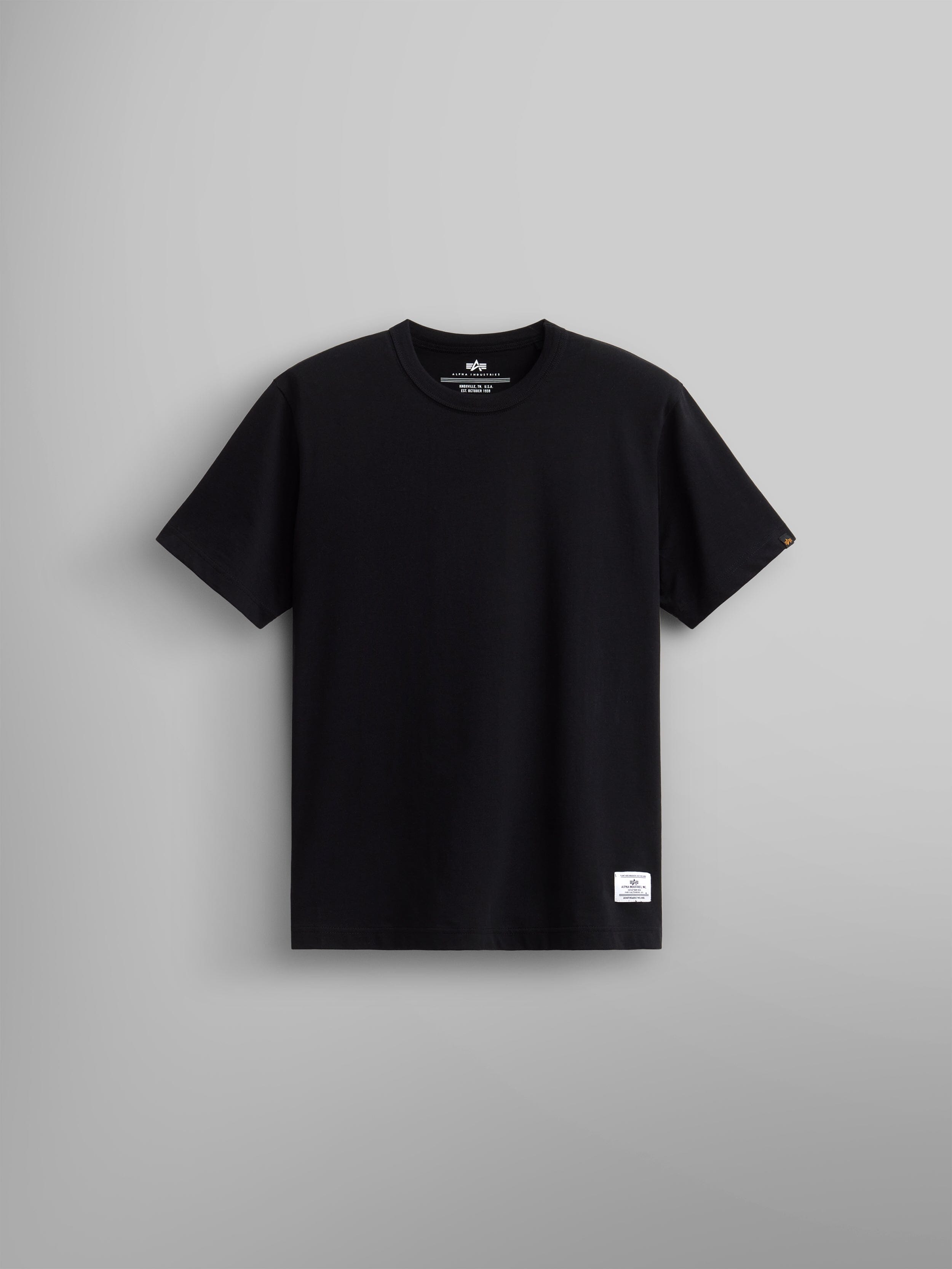Alpha Industries Essential Tee in black cotton with short sleeves, crew neck, and small white label near the bottom hem.