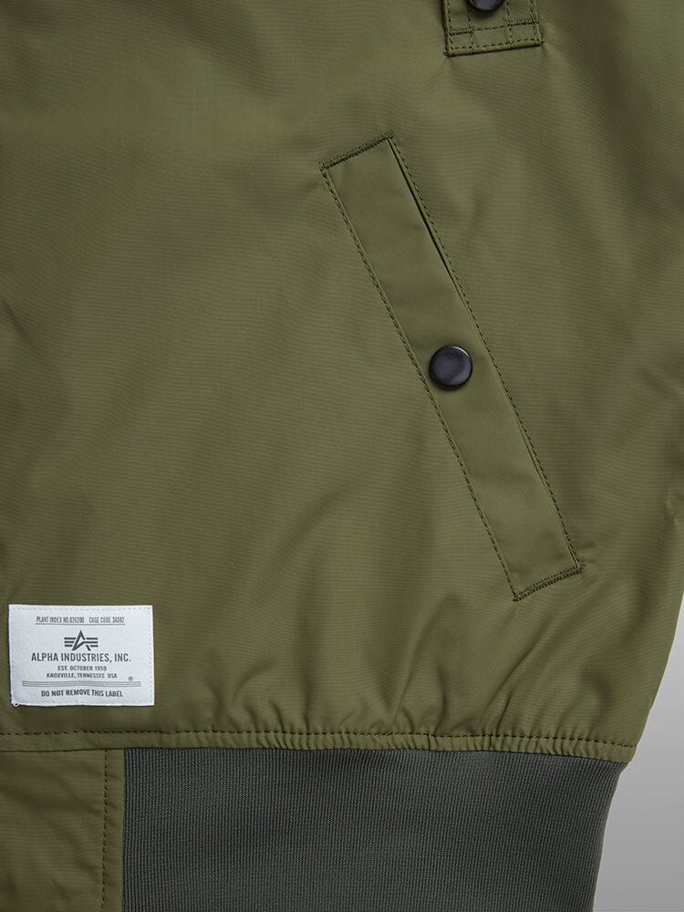 L-2B Skymaster Gen Ii Bomber Jacket by Alpha Industries, olive green, slanted front pocket with black snap buttons, ribbed hem, oxygen tab details, white Alpha Industries label at bottom.