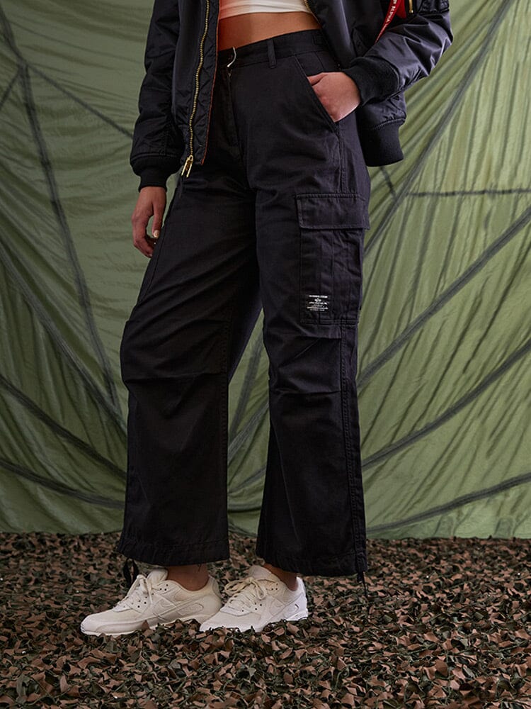 Alpha Industries M-65 Cargo Pant Womens in black, with cargo pockets; white sneakers; white crop top; black jacket.