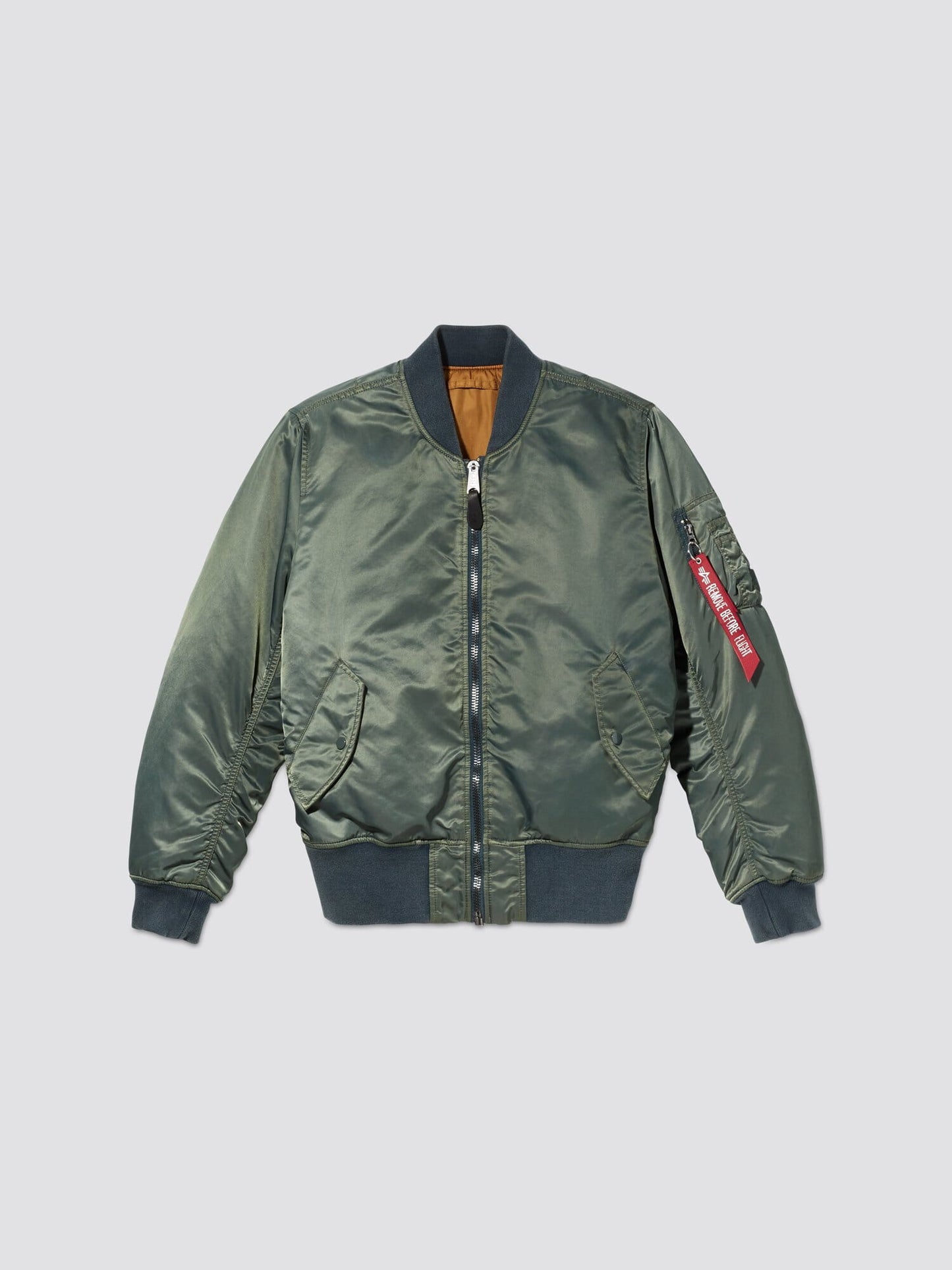 Teal MA-1 Battlewash Bomber Jacket from Alpha Industries, Inc. featuring a zipper, two side pockets, and a red "Remove Before Flight" tag on the sleeve. This garment-wash piece offers both style and comfort.