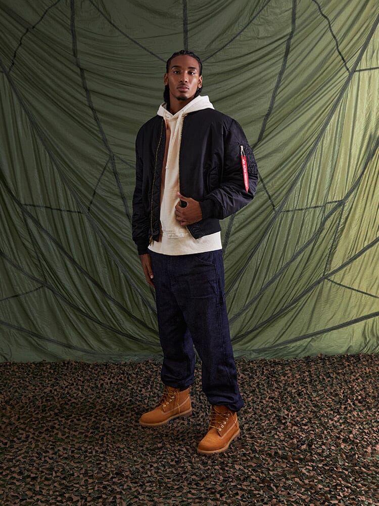 Alpha Industries MA-1 Bomber Jacket in black flight nylon, cream hoodie, dark cargo pants, tan boots.