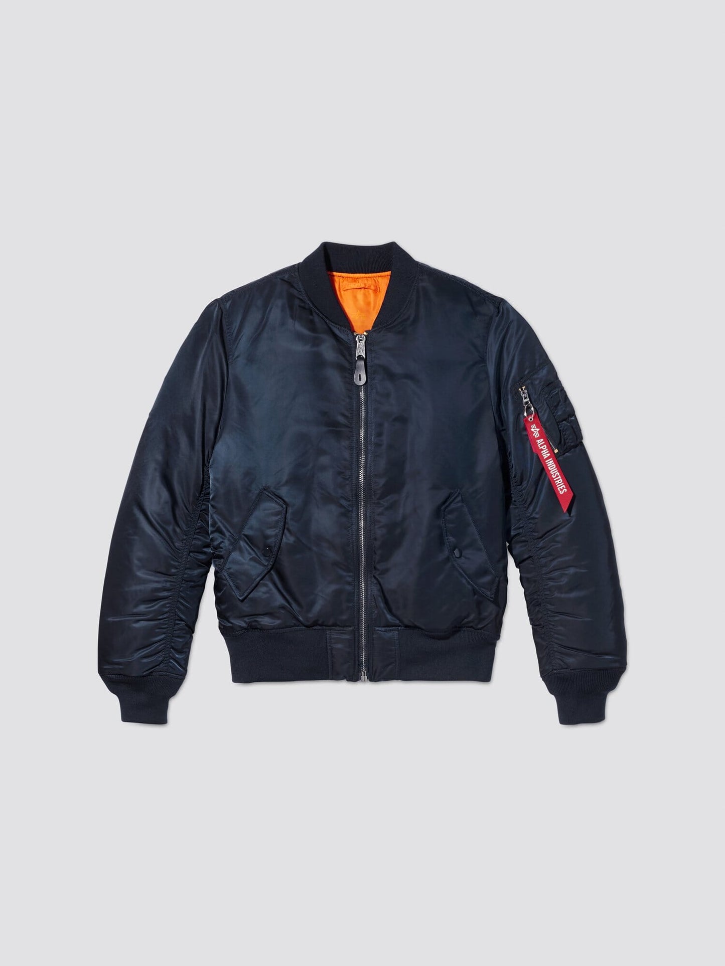 Front flat-lay view of replica blue Alpha Industries MA-1 Bomber Jacket Slim Fit showing orange lining and sleeve pocket with red tag.