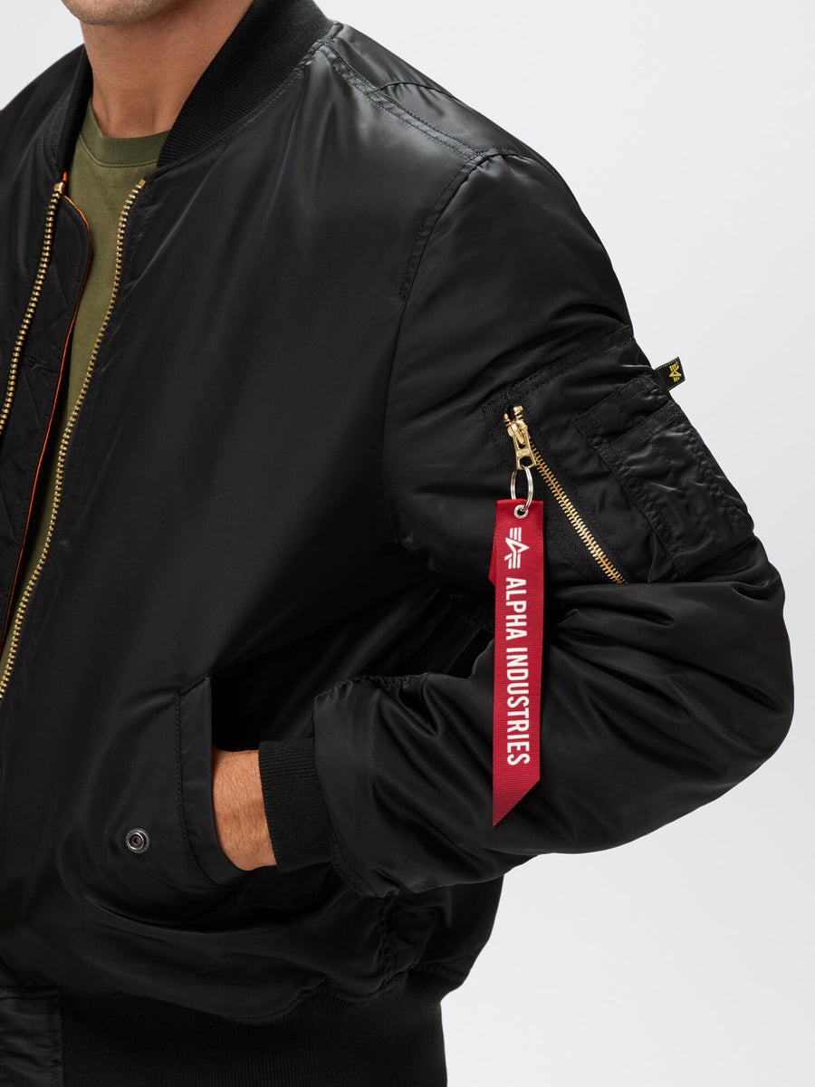 Close-up view of black Alpha Industries MA-1 Bomber Jacket Slim Fit highlighting sleeve pocket with red “Remove Before Flight” tag.
