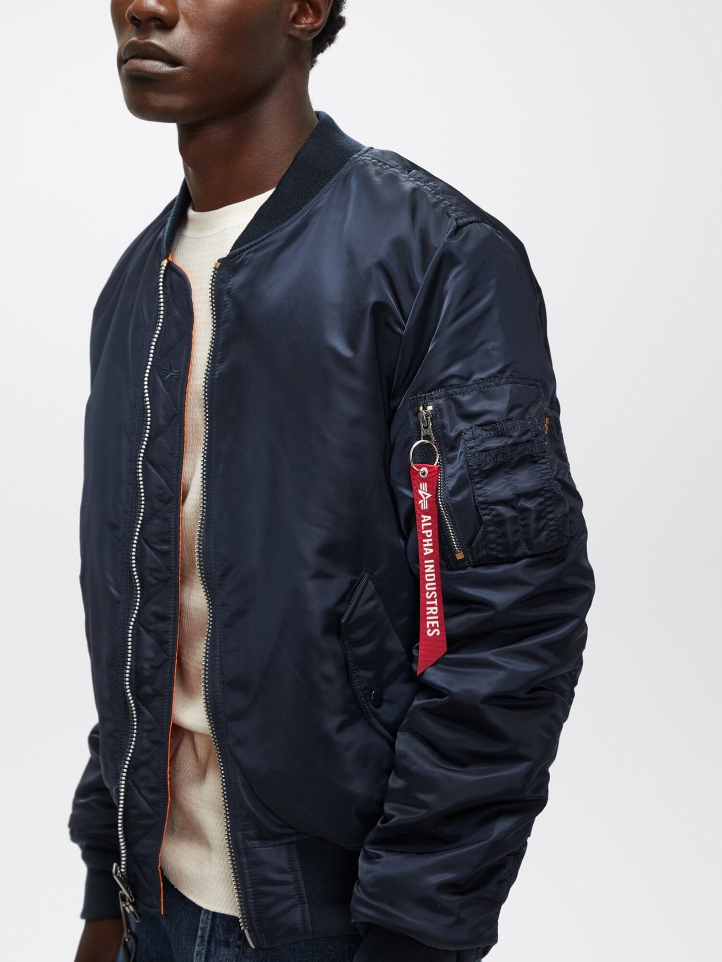 Close-up view of replica blue Alpha Industries MA-1 Bomber Jacket Slim Fit highlighting sleeve pocket with red “Remove Before Flight” tag.