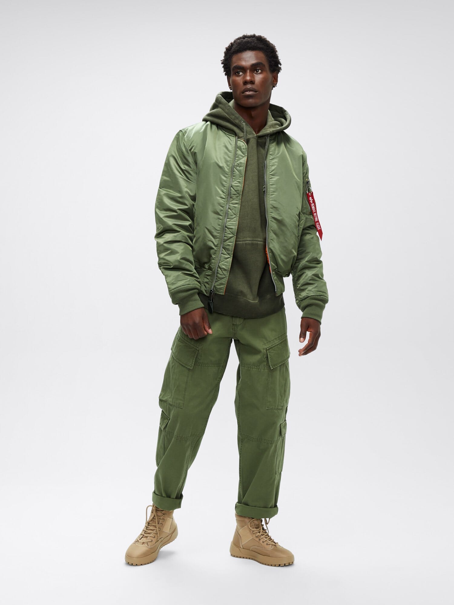 Three-quarter full-body front view of sage green Alpha Industries MA-1 Bomber Jacket Slim Fit showing ribbed cuffs, waistband, and red sleeve tag.