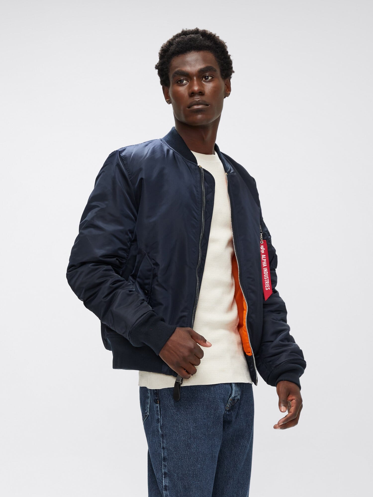 Three-quarter front view of replica blue Alpha Industries MA-1 Bomber Jacket Slim Fit highlighting orange lining and sleeve pocket with red tag.