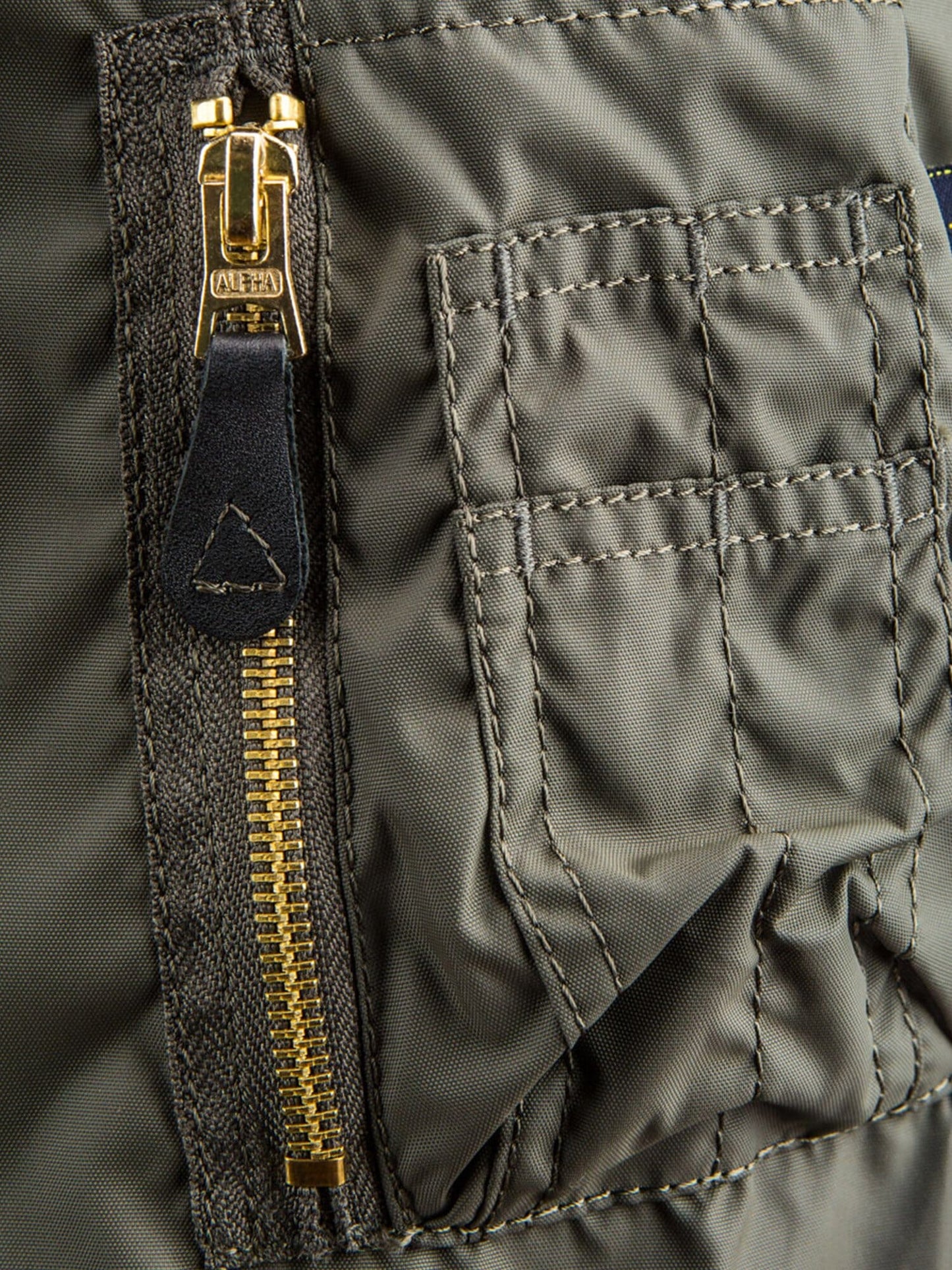 Alpha Industries MA-1 Skymaster Bomber Jacket in green, gold zipper, leather pull tab, stitched rectangular pocket with flap.