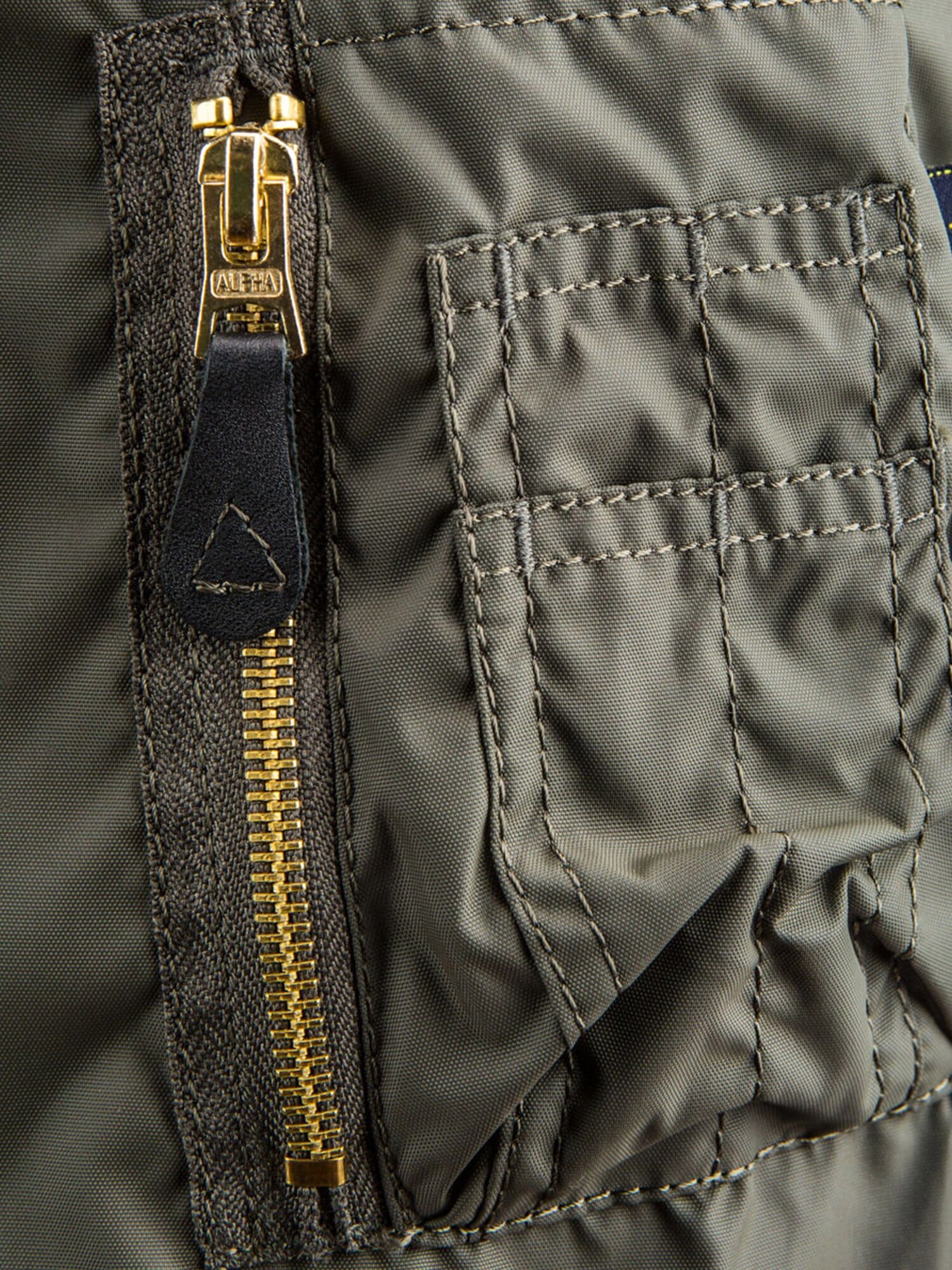 Alpha Industries MA-1 Skymaster Bomber Jacket in green, gold zipper, leather pull tab, stitched rectangular pocket with flap.