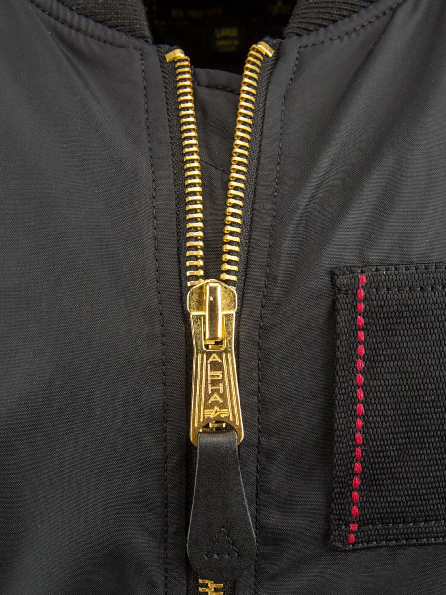 Alpha Industries MA-1 Skymaster Bomber Jacket, gold metal zipper, visible stitching, small right-side pocket with red thread.