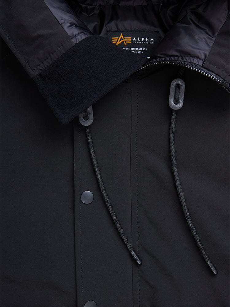 Close-up of a black N-2B Altitude Parka highlighting its collar, zipper, drawstrings, and snap buttons. The inside label displays Alpha Industries with care instructions.