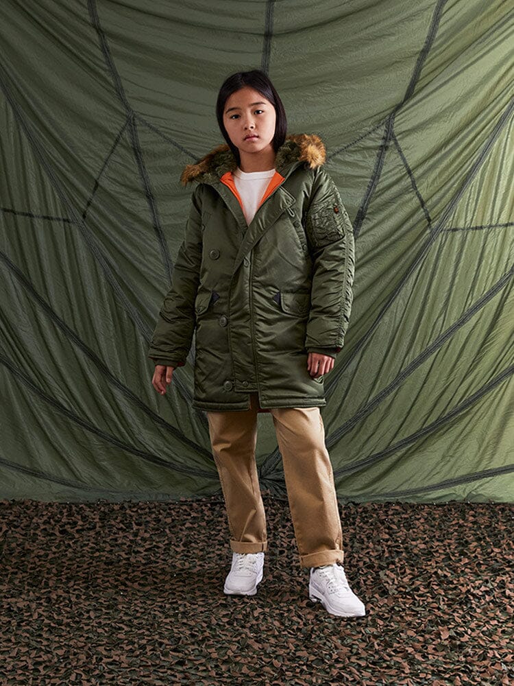 Alpha Industries N-3B Parka Youth, fur-lined hood, khaki color, water-resistant material, front zipper and button closures.