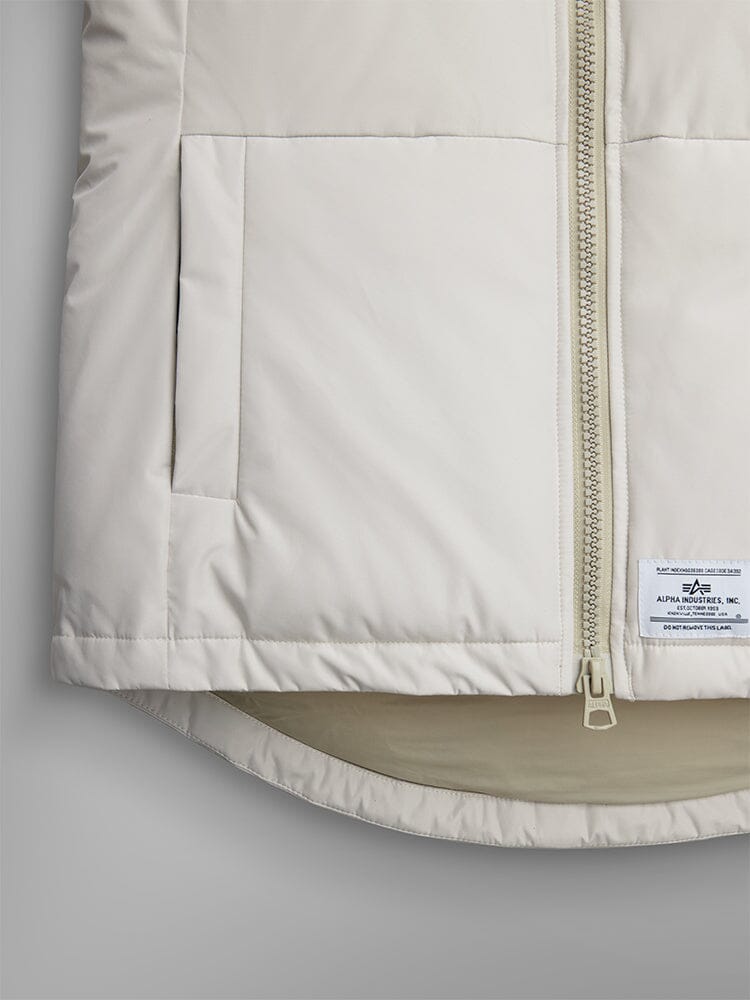 Alpha Industries Short Parka W, light color, zipper, utility pockets, small rectangular label near bottom hem.
